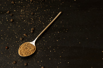 Teaspoon ground mixture of peppers on a black background