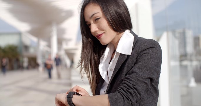 Attractive woman checking the time on her wristwatch as she sits on a bench in town waiting for a rendezvous