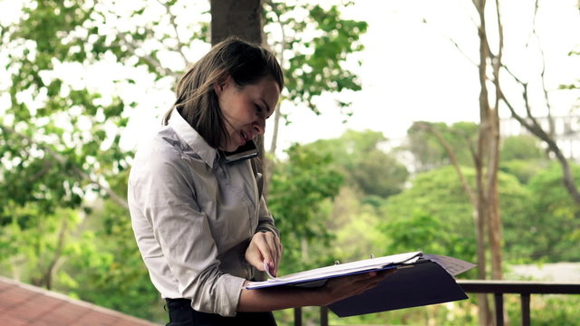 Angry businesswoman with documents talking on cellphone while standing on terrace
