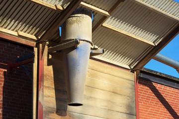 A sawdust outlet on the side of a building. Outlet comes from above in the steel roof and piles of sawdust accumulate underneath.