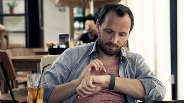 Young man with smartwatch drinking juice in cafe
