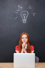 Pensive woman usind laptop and thinking over chalkboard backgroud