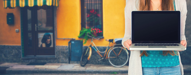 Junge Frau steht mit einem Notebook vor einem Laden 