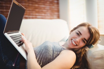 Pretty woman lying on the couch using her laptop