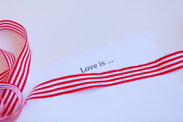 Paper with words Love is and ribbon