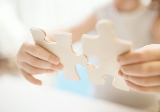  Child girl holding  two big wooden puzzle pieces. Hands connecting jigsaw puzzle. Close up photo with small dof. Education and learning concept.