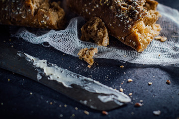Torn baguette from dark bread with seeds .and a knife smeared with butter.