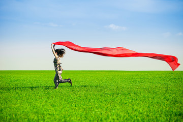 Beautiful young woman jumping on a green meadow with colored tissue