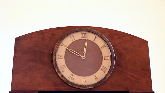 Old vintage wooden mantel clock with brass roman numerals against white background. Both hands rotating fast