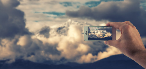 Männliche Hand haltet ein weißes Smartphone und fotografiert damit ein Bergpanorama