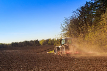 Naklejka premium cultivator operates on ploughed field near spring forest