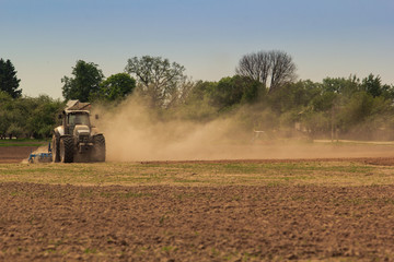 Fototapeta premium cultivator operates on ploughed field raises dust in spring