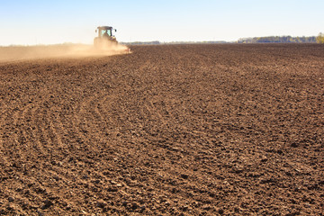 cultivator operates on ploughed field near spring forest