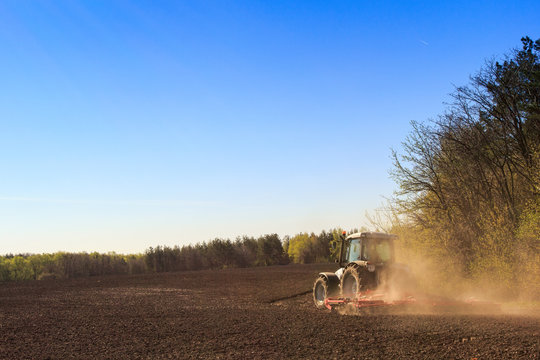 cultivator operates on ploughed field near spring forest