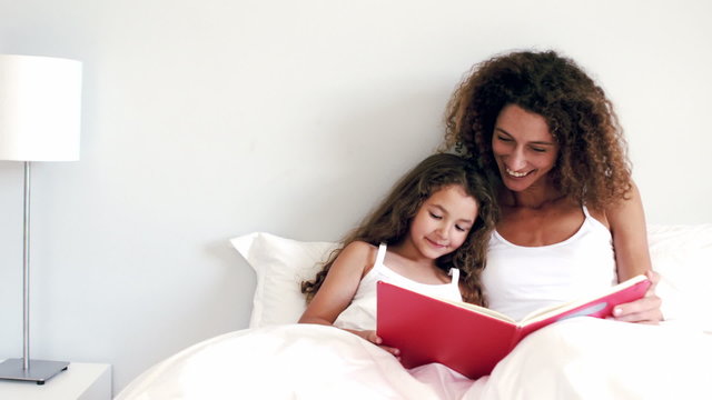 Mother and daughter reading a book together on their bed