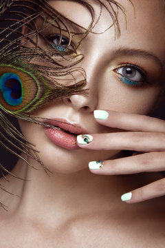 Beautiful girl with bright makeup, manicure design and peacock feather on her face. Art nails.
