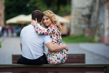 Happy, stylish newlywed couple posing on wooden bench in town