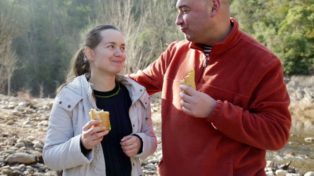 Handsome man and cheerful woman eating sandwitches at picnic outdoors