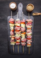 raw kebabs with pork, vegetables and fruit on vintage cutting board with spices on wooden rustic background top view close up