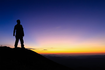 Fototapeta na wymiar Silhouette of man standing on the top of mountain to enjoy colourful sky
