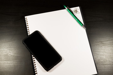Blank notebook and smartphone with pencil on wooden table. The view from the top