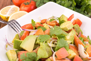 Fresh avocado Salad  with tomatoes, purple onion on the white dish. Healthyt food concept