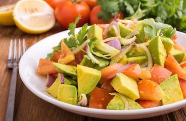 Fresh avocado Salad  with tomatoes, purple onion on the white dish. Healthyt food concept