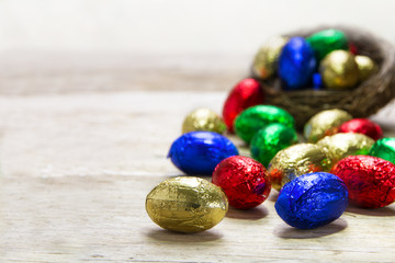 colorful chocolate easter eggs rolling out of a nest on a rustic