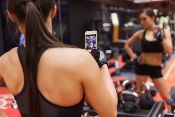 woman with smartphone taking mirror selfie in gym