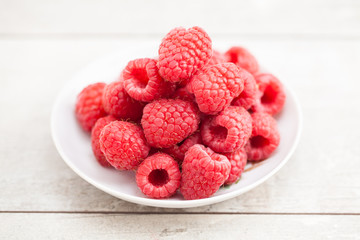 fresh ripe raspberries in white saucer on wood table