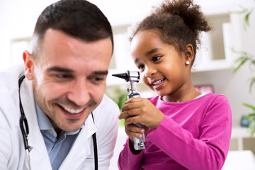Little african girl holding otoscope and playing with pediatrici