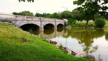 Fototapeta na wymiar Old three arch bridge with green grass, trees and water in Delaware park, Buffalo New York