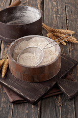 Flour in a wooden bowl with sieve on vintage board