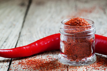 Ground hot red pepper in a glass jar and fresh chili peppers on