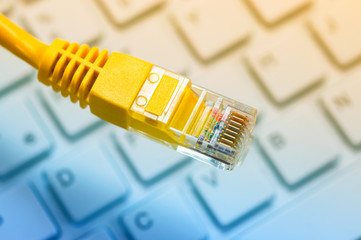 Macro of a yellow network cable in front of a computer keyboard