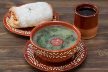 typical portuguese soup caldo verde with bread with chourico and red wine on brown wooden background