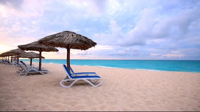 Beautiful pink sand beach with rows of chairs under the shade of coconut palm umbrellas in tropical resort.
