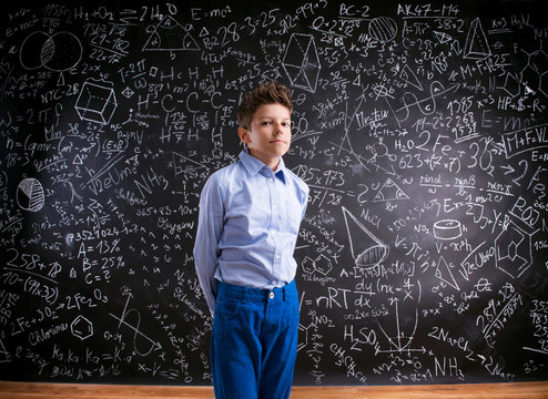 Boy against big blackboard with mathematical symbols and formula