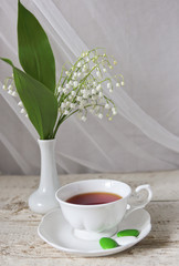 cup of tea and a bouquet of lilies of the valley in the vase