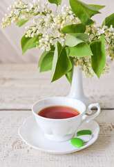 cup of tea and a bouquet of white lilac in the vase
