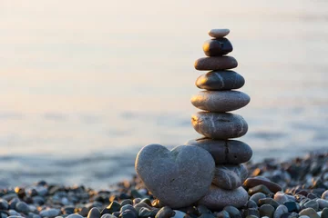 Rolgordijnen Grey stone in shape of heart in front of balanced stones on still water background © dsdesigner