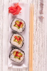 Japanese food. Vegetable rolls with ginger and chopsticks on white plate, white wooden background. Top view