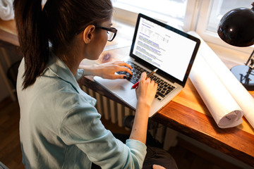 Young female blogger working at home.She sitting in her working room and typing something on laptop.