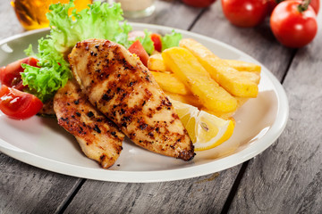 Grilled chicken breasts served with fries and fresh salad