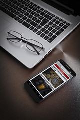 news on smartphone screen, eyeglasses on laptop computer