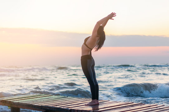 Enlightened Young woman relaxing on the beach, meditating in asana hasta uttanasana, with hands In Namaste gesture at sunset or sunrise, close up