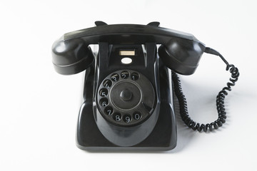 Old black dial phone on a white background, front view, horn on the hook. 