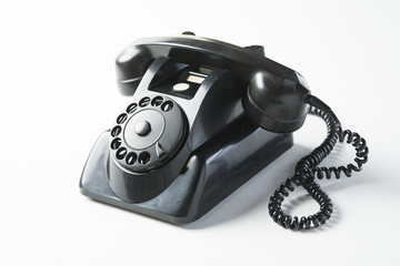 Old black dial phone on a white background, edgewise, horn on the hook.