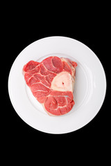 one piece of raw beef meat with the bone in the middle on black background
