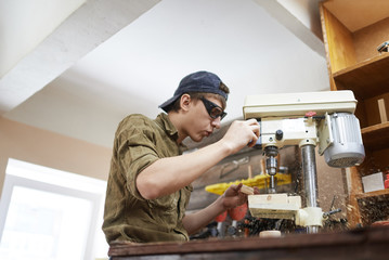 young carpenter blow away chips from the machine, drill, In goggles